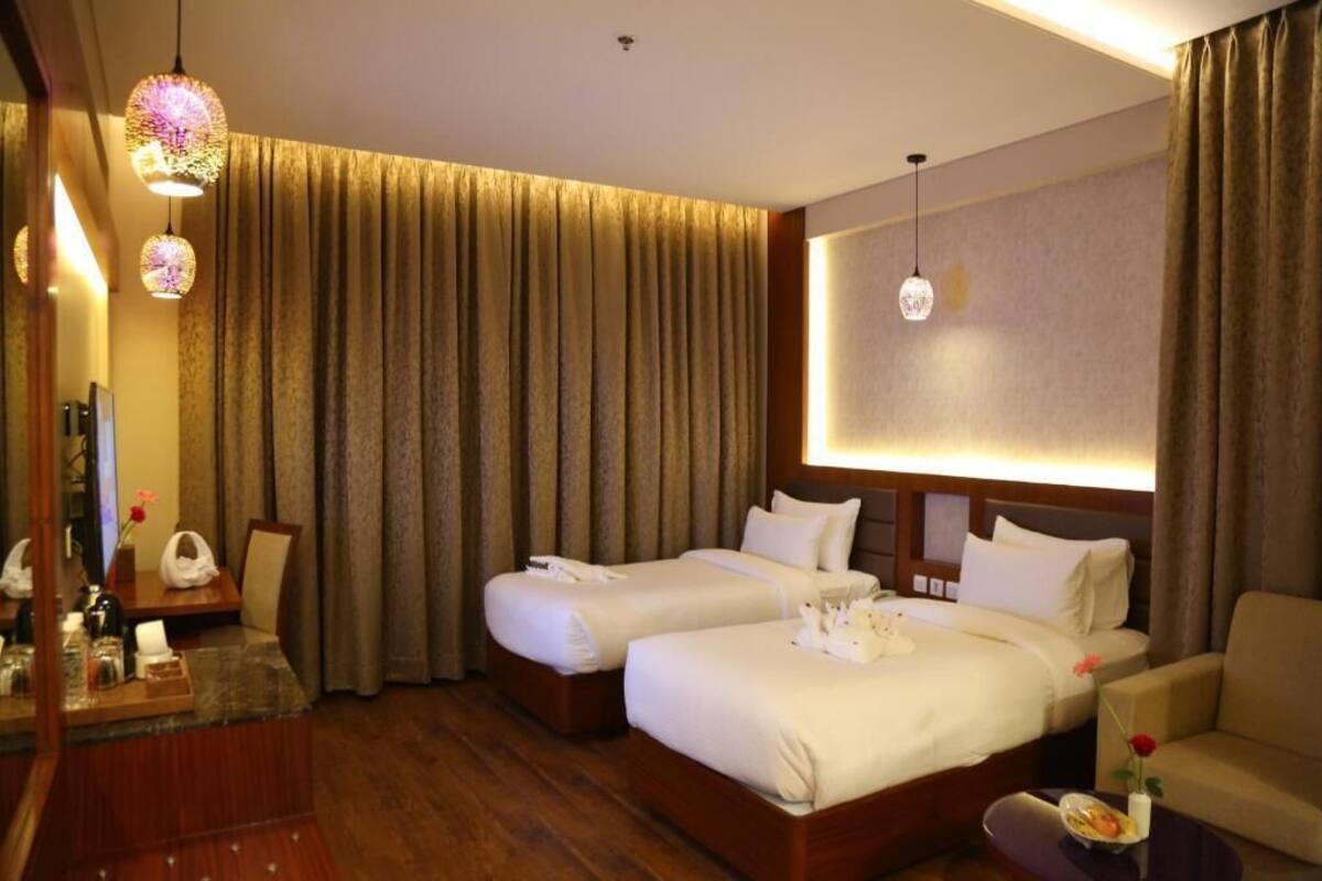 A hotel room with two beds, a desk, a chair, and a large window with curtains.