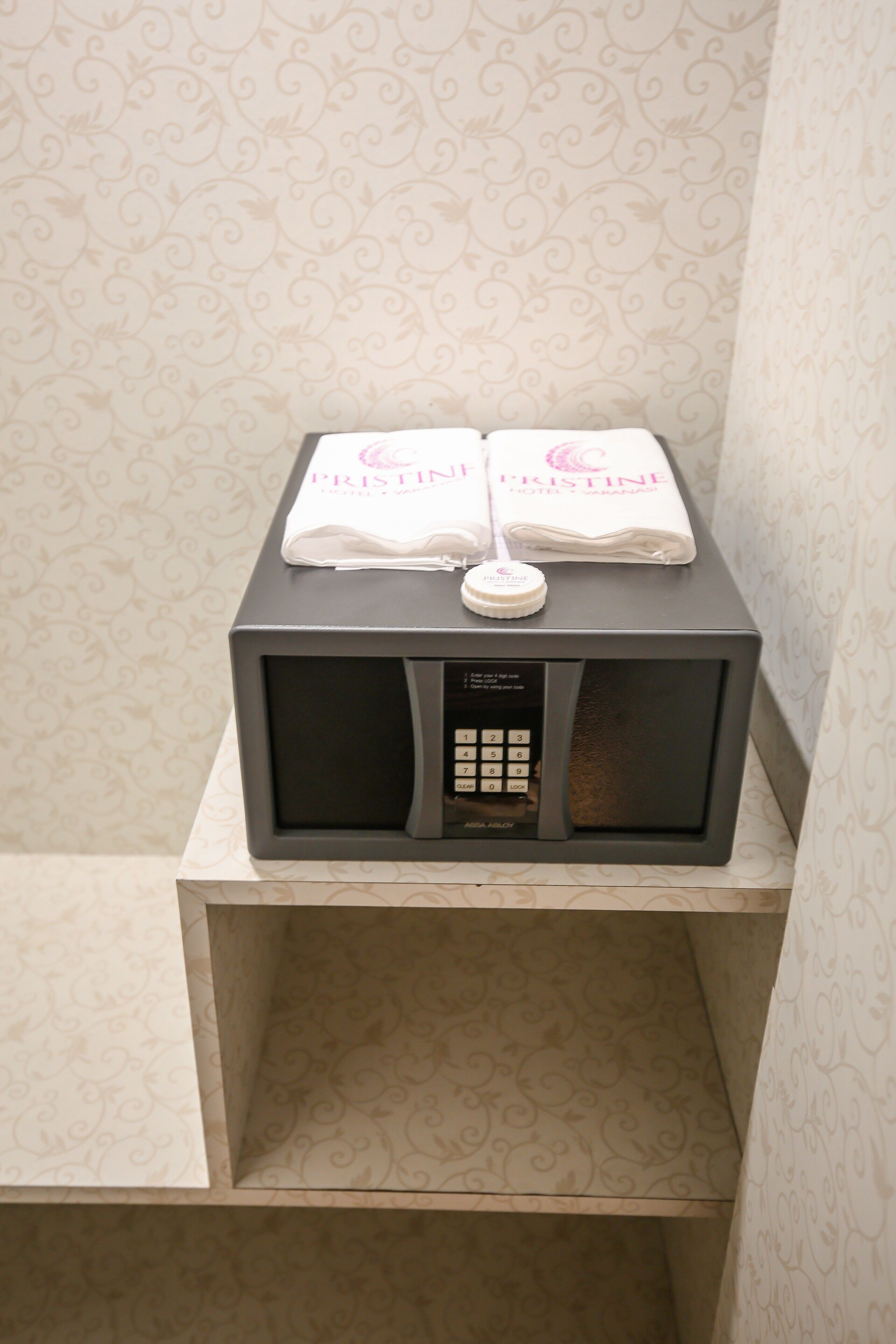 A microwave with a control panel and a small bottle on top, placed on a shelf in a room with patterned wallpaper.