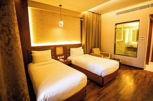Habitación de hotel con dos camas, una mesita de noche, una silla, un espejo grande y suelo de madera.
