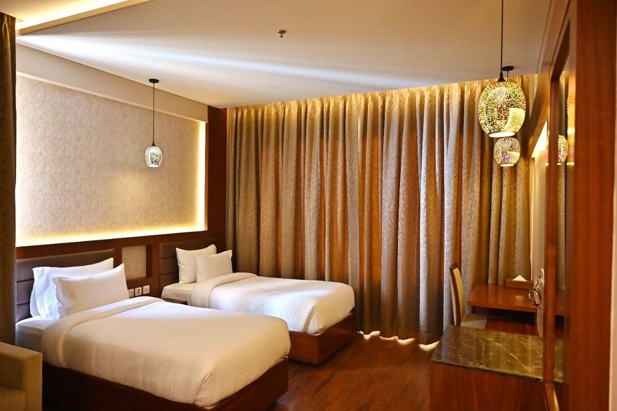 A hotel room with two beds, a wooden headboard, a small table, and a curtain with a golden pattern.