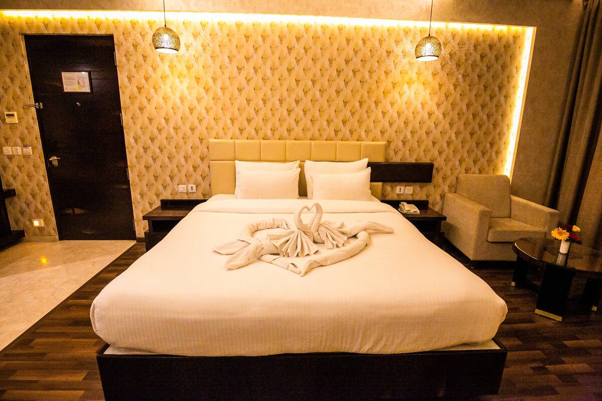 A hotel room with a large bed, a headboard, a nightstand, a chair, and a small table with a vase.