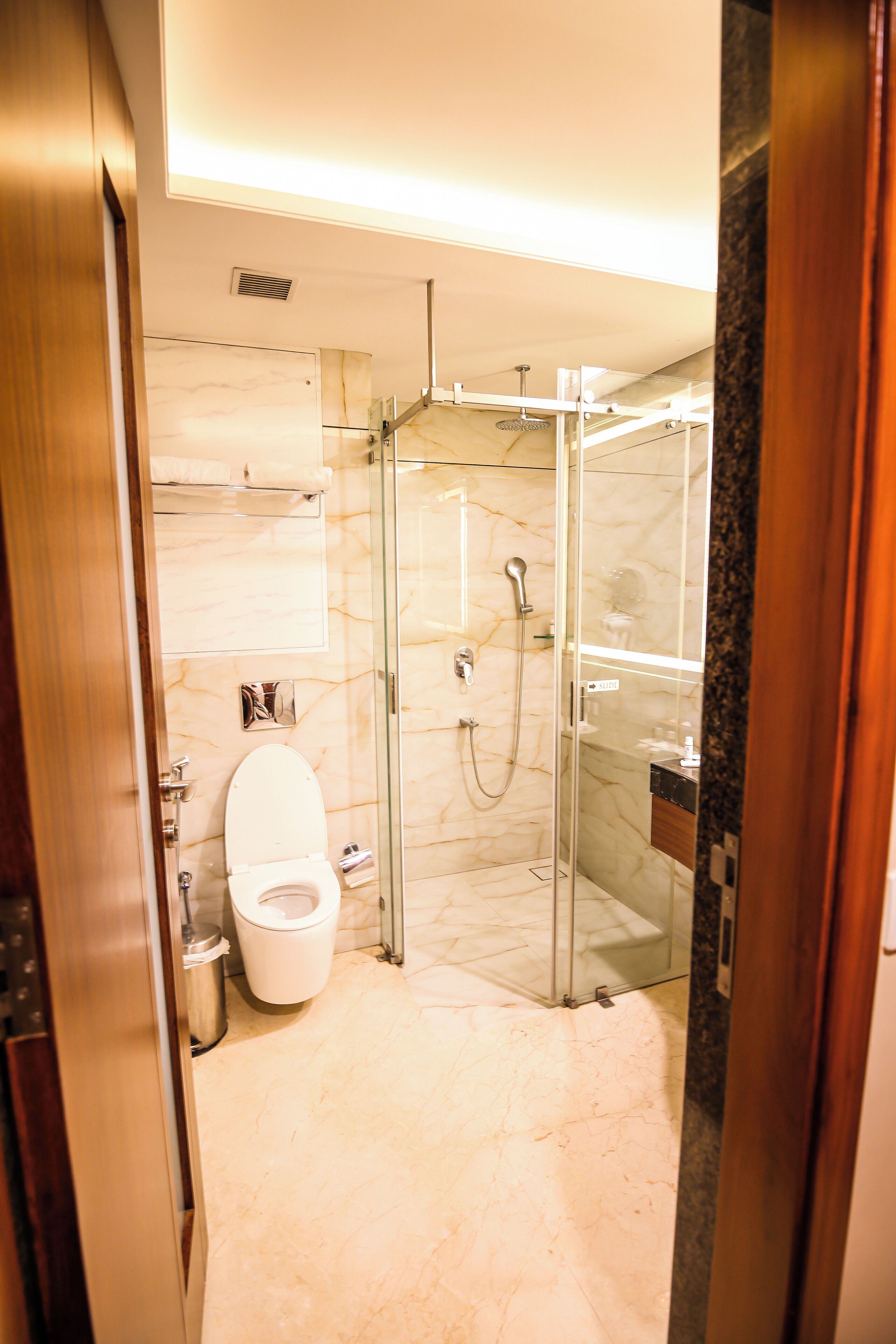 A modern bathroom with a glass-enclosed shower, a toilet, and a marble floor.
