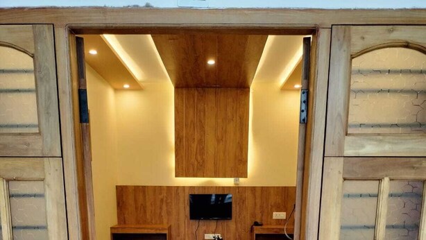 A room with a wooden door, a television mounted on the wall, a blue sofa, and a patterned rug. - Orange Valley Plantation Holiday Resort Coorg (Virajpet)