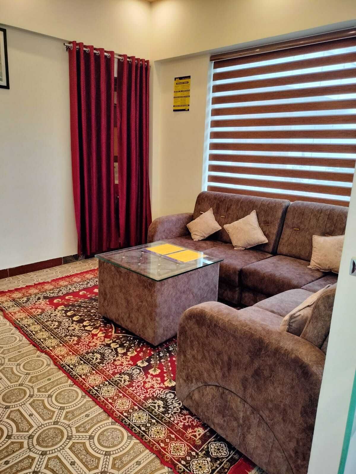 Een woonkamer met een bruine bank, een glazen salontafel en een kamerbreed tapijt met een patroon.