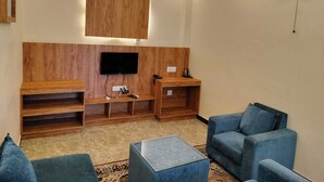 A living room with a wooden accent wall, a mounted TV, a fan, and blue furniture. - Orange Valley Plantation Holiday Resort Coorg (Virajpet)