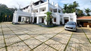 A large, multi-story white building with a spacious paved courtyard, a car parked in front, and a clear sky. - Orange Valley Plantation Holiday Resort Coorg (Virajpet)