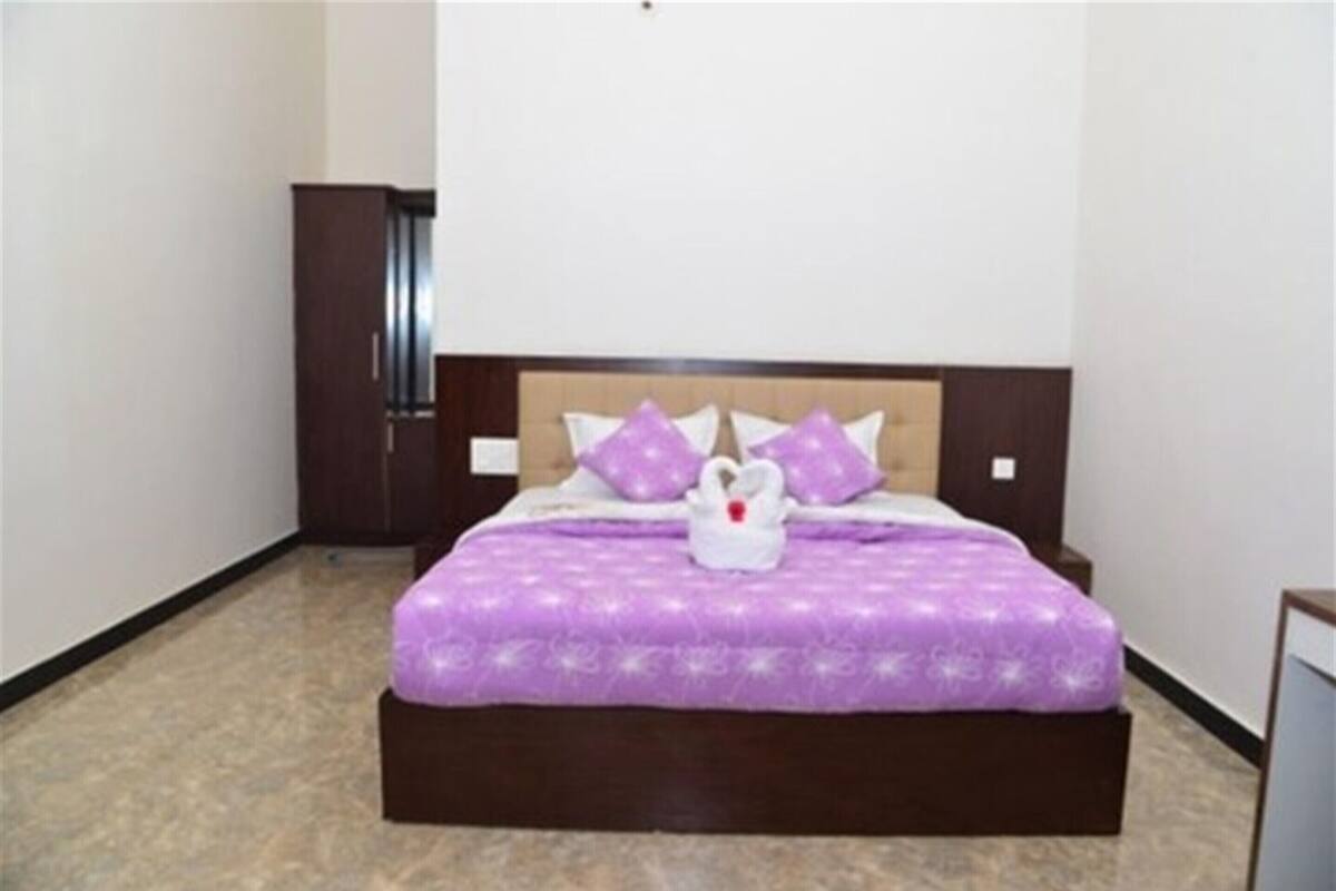 Un lit bien fait, avec une couvre-lit violette et des coussins assortis, une tête de lit en bois et une petite décoration représentant un cygne blanc posée sur le lit.