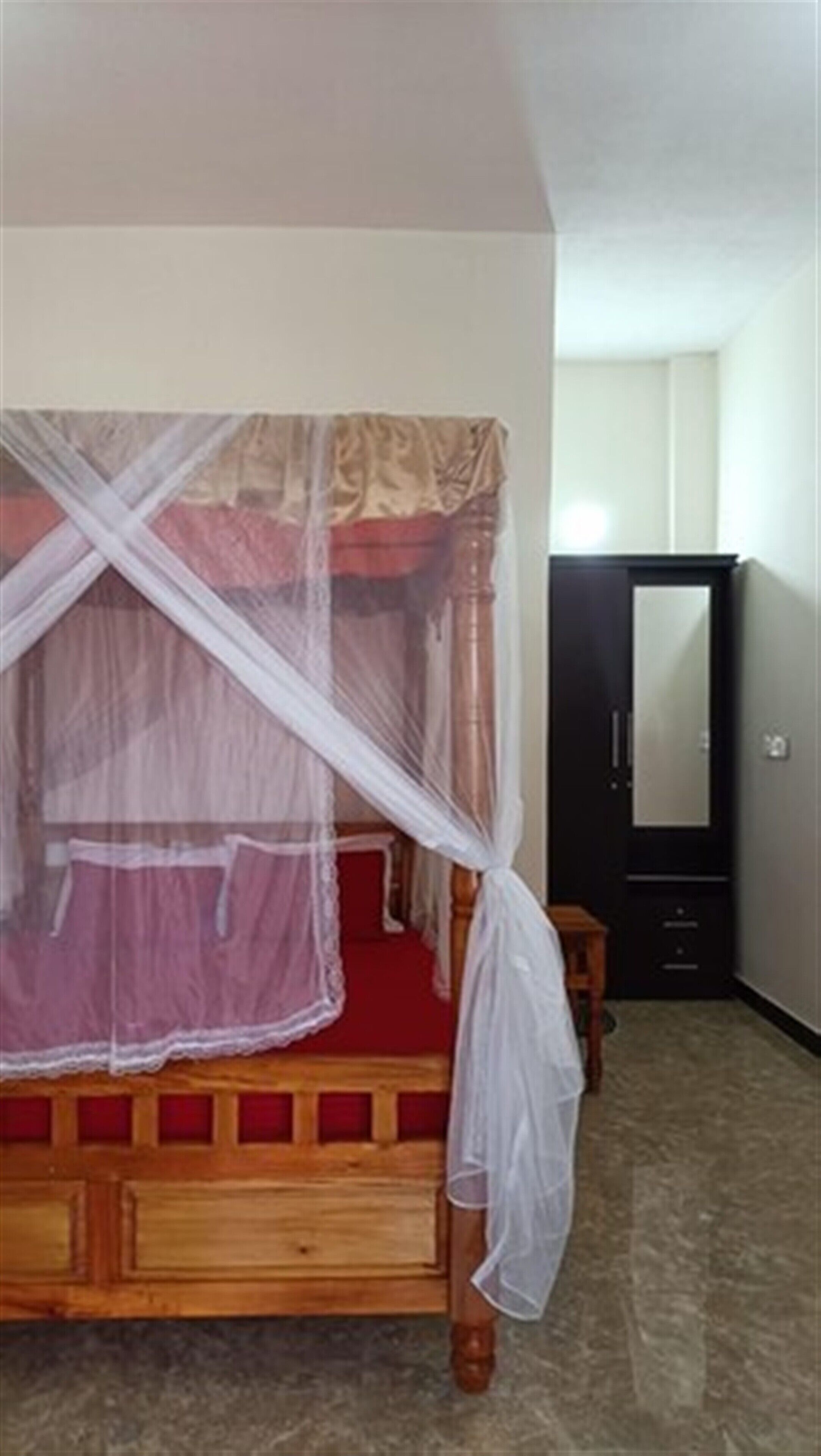 A bedroom with a wooden bed, a canopy, a wardrobe, and a mirror.