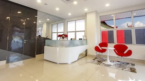 Un'area reception moderna con un bancone in vetro, un'addetta alla reception e sedie rosse.