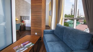Una camera d'albergo moderna con un'ampia finestra, un divano blu, un tavolino in legno e un letto con una testiera grigia.