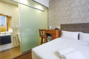 A hotel room with a bed, a desk, a chair, a shower, and a bathroom with a toilet and sink. - CitiVilla Penang (George Town)