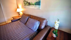 A hotel room with a bed, a nightstand with a lamp, a painting on the wall, and a potted orchid on a side table. - 1-bedroom private home just 4 minutes to Lucas Oil Stadium (Indianapolis)
