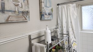 A bathroom with a shower curtain, a towel rack, and a shelf with toiletries. - 1-bedroom private home just 4 minutes to Lucas Oil Stadium (Indianapolis)