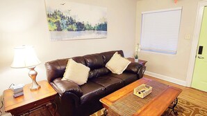 A living room with a leather sofa, a wooden coffee table, a lamp, and a door with a window. - 1-bedroom private home just 4 minutes to Lucas Oil Stadium (Indianapolis)