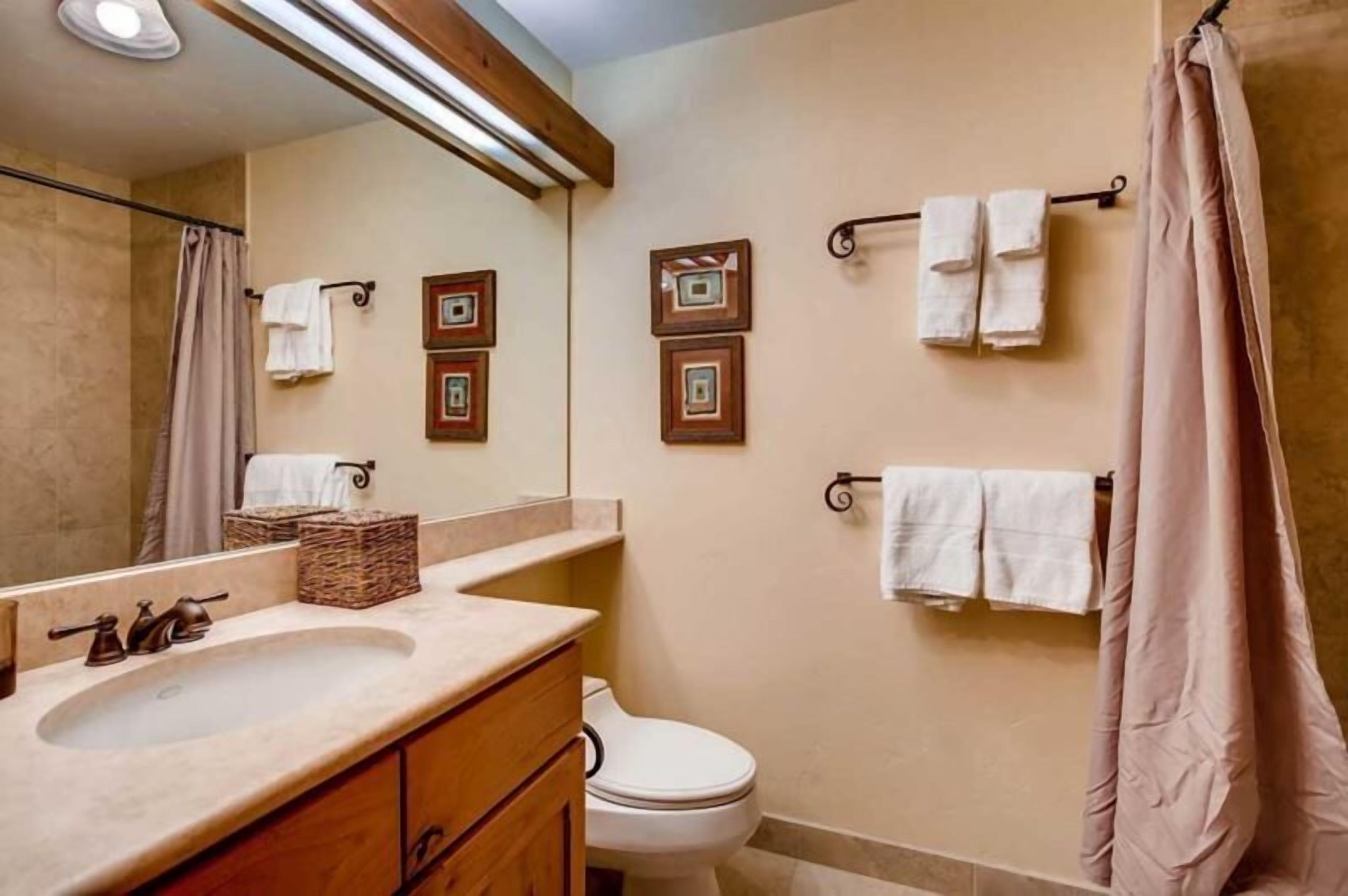 Une salle de bain avec un lavabo, un miroir et des toilettes. Des serviettes sont accrochées à des crochets et il y a un rideau de douche.