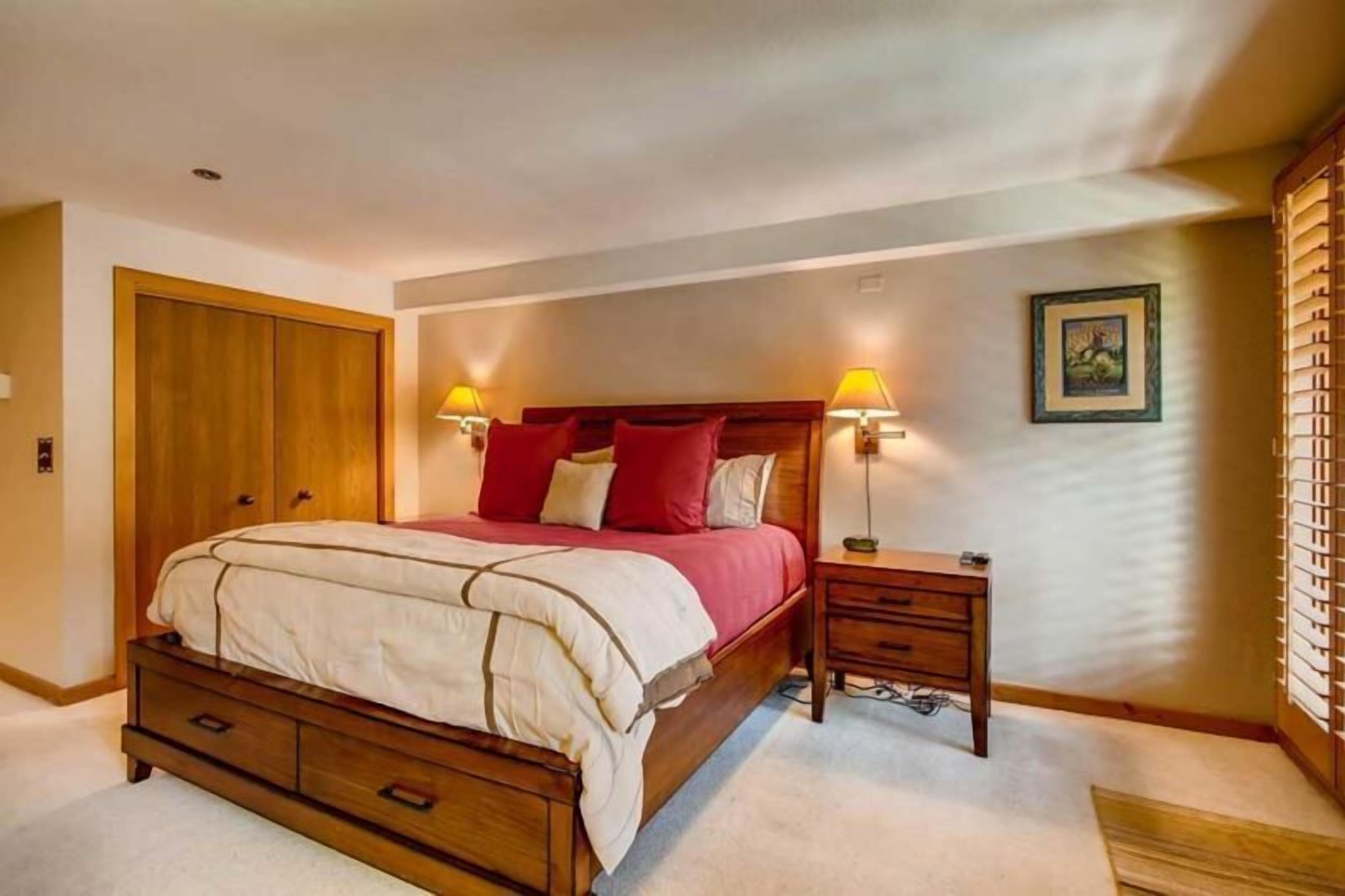 Une chambre à coucher avec un lit en bois, des tables de chevet avec des lampes, une armoire et un tableau encadré au mur.