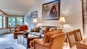Ein gemütliches Wohnzimmer mit einer Couch, Sesseln, einem Couchtisch und Kunstwerken an den Wänden.