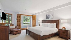 Un dormitorio con una cama grande, televisión, escritorio, silla y ventana con persianas.
