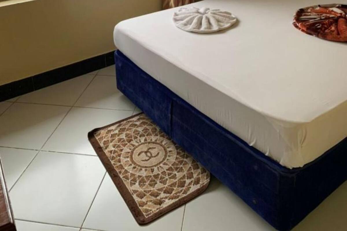 Habitación de hotel con cama, ventana con vista a edificios, alfombra estampada y un adorno en la cama.