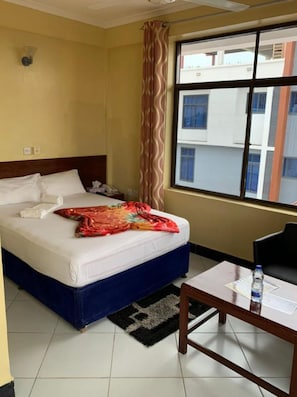A hotel room with a bed, a desk, and a window with a view of buildings outside.