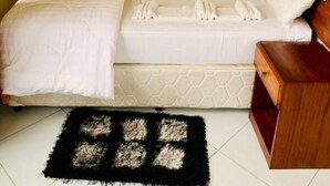 Un lit simple avec un matelas blanc et des oreillers assortis, une table de chevet en bois et un tapis noir à motifs géométriques.
