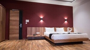 A modern hotel room with a wooden headboard, a wooden bench, a bed with white bedding, and two wall-mounted lights. - TGN SUITS - HOTEL (Raipur)