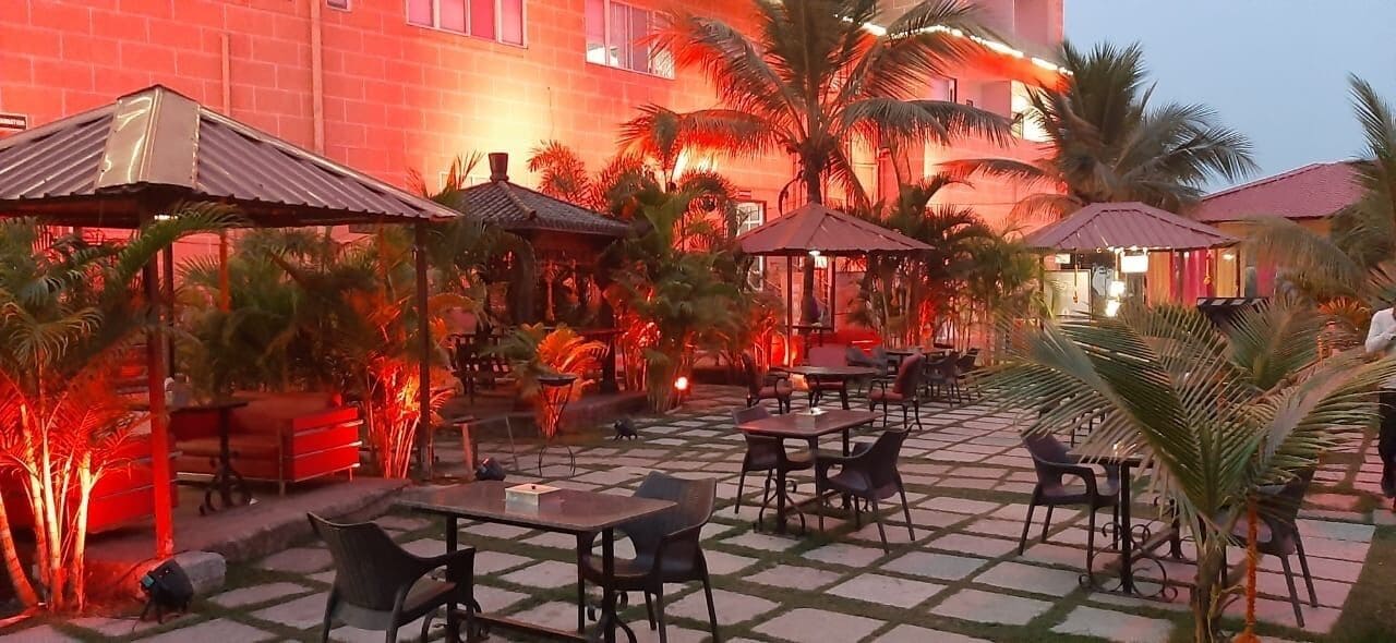 Un patio al aire libre con mesas y sillas, palmeras y un edificio al fondo.