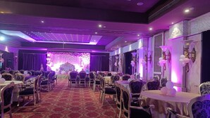 A banquet hall with round tables and chairs, a red carpet, and purple lighting. - TGN SUITS - HOTEL (Raipur)