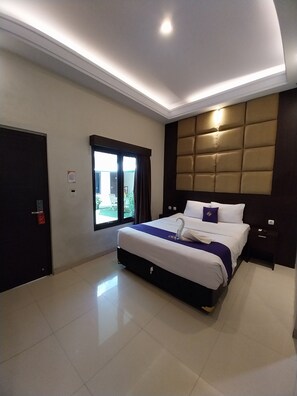 A hotel room with a large bed, a headboard with a padded design, a window with curtains, and a door with a lock.
