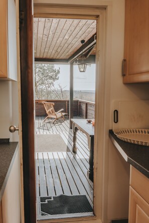 Eine Holzterrasse mit Tisch und Stühlen, Blick auf Bäume und eine entfernte Landschaft.
