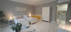 A modern bedroom with two beds, a wardrobe, a bedside table with a lamp, and a dining area with a table set for two. - Camille Apartments (Budapest)
