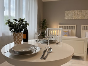A dining table set with plates, cutlery, and wine glasses, with a potted plant and a bottle of wine on the table. - Camille Apartments (Budapest)