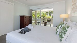 Una habitación de hotel con cama, cómoda, balcón con sillas y mesa con botella y vasos.