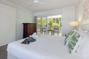 Relax in a serene space with a large bed, wooden dresser, and a window offering a view of lush greenery.