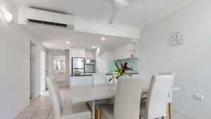 Una cocina moderna con armarios blancos, una isla central y un comedor con una mesa y sillas blancas.