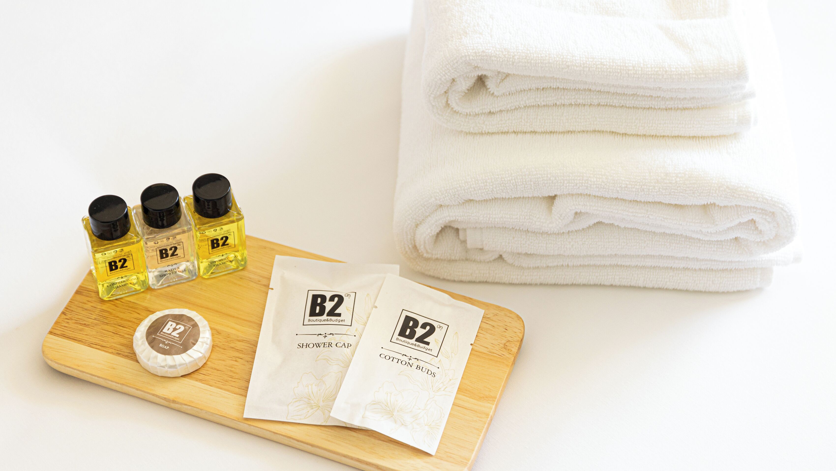 A wooden tray with B2 branded shower cap, cotton buds, and two bottles of B2 shower gel.