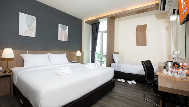 Une chambre d’hôtel avec un grand lit, un lit plus petit, un bureau avec une chaise et une fenêtre avec des rideaux.