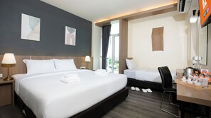 Une chambre d’hôtel avec un grand lit, un lit plus petit, un bureau avec une chaise et une fenêtre avec des rideaux.