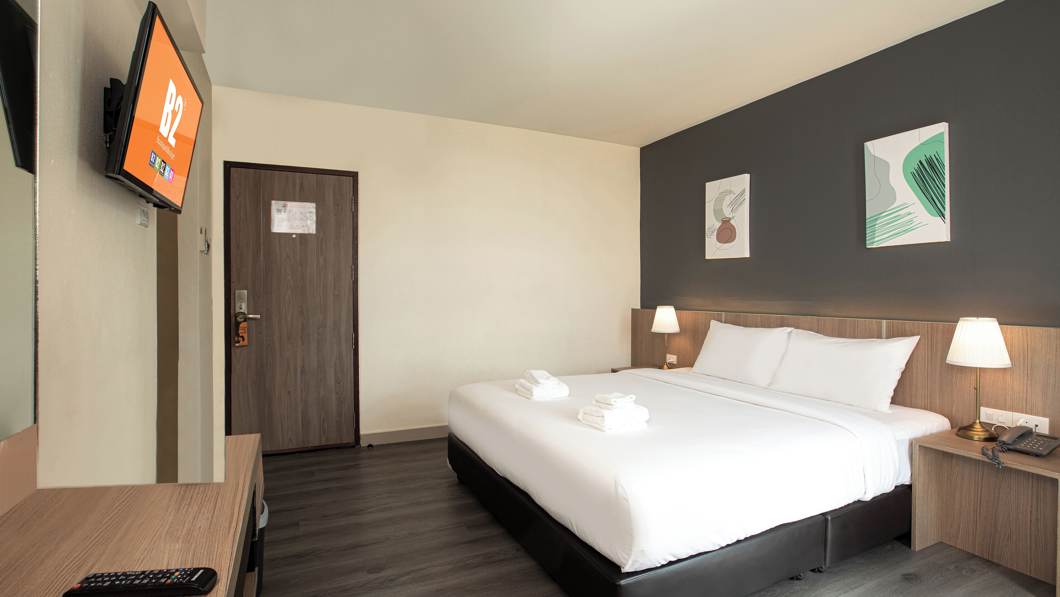 A hotel room with a bed, bedside lamps, a TV on the wall, and a desk with a remote control.