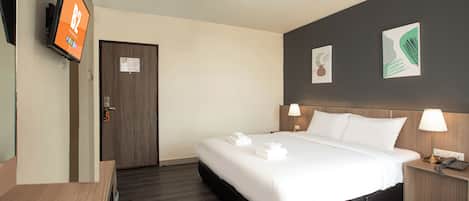 Habitación de hotel con cama, lámparas de noche, televisor en la pared y escritorio con control remoto.