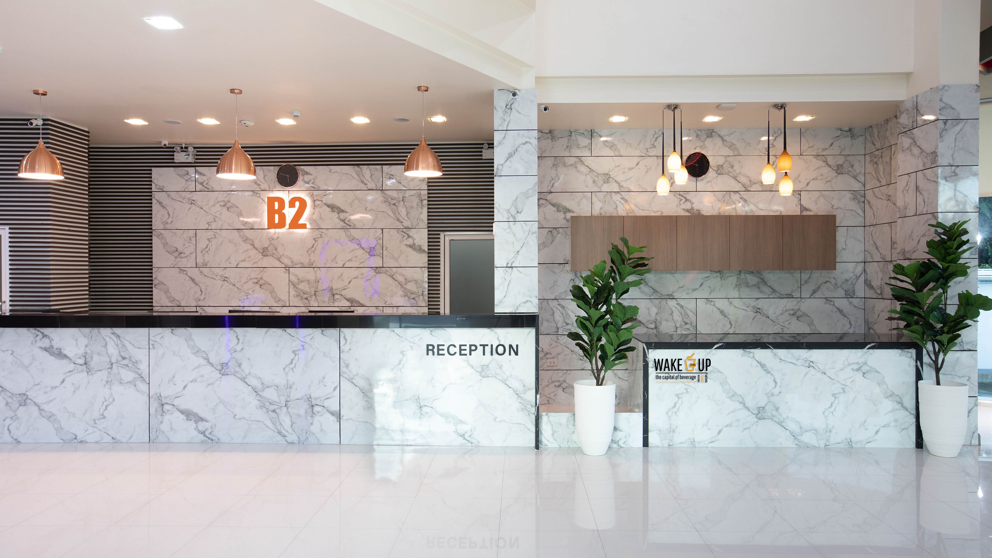 A reception area with a marble wall, a reception desk labeled "RECEPTION," and a sign that reads "WAKE UP the capital of beverage."