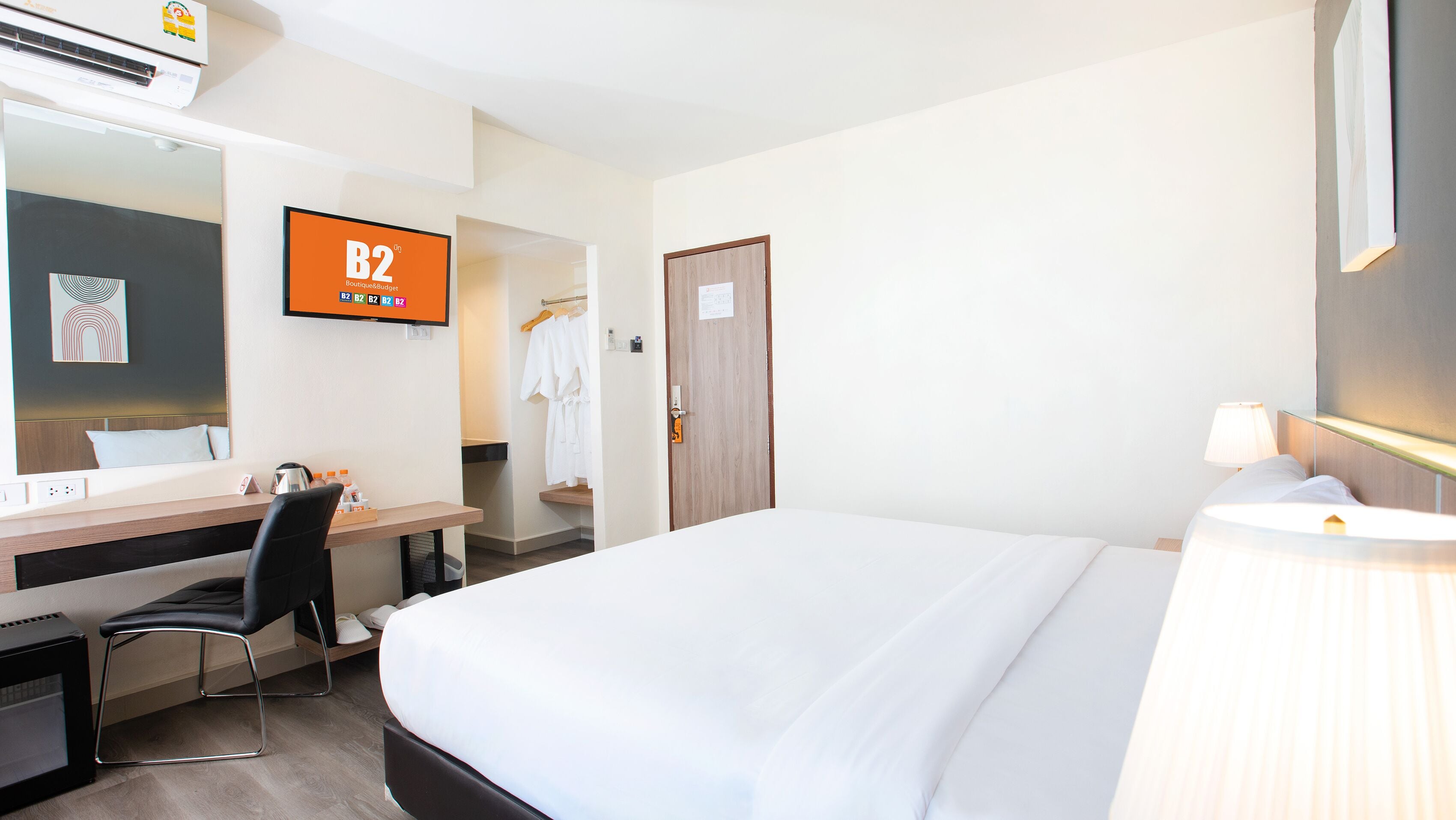 A hotel room with a bed, desk, chair, and a television displaying 'B2 Boutique Budget'.