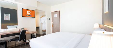 A hotel room with a bed, desk, chair, and a television displaying 'B2 Boutique Budget'.