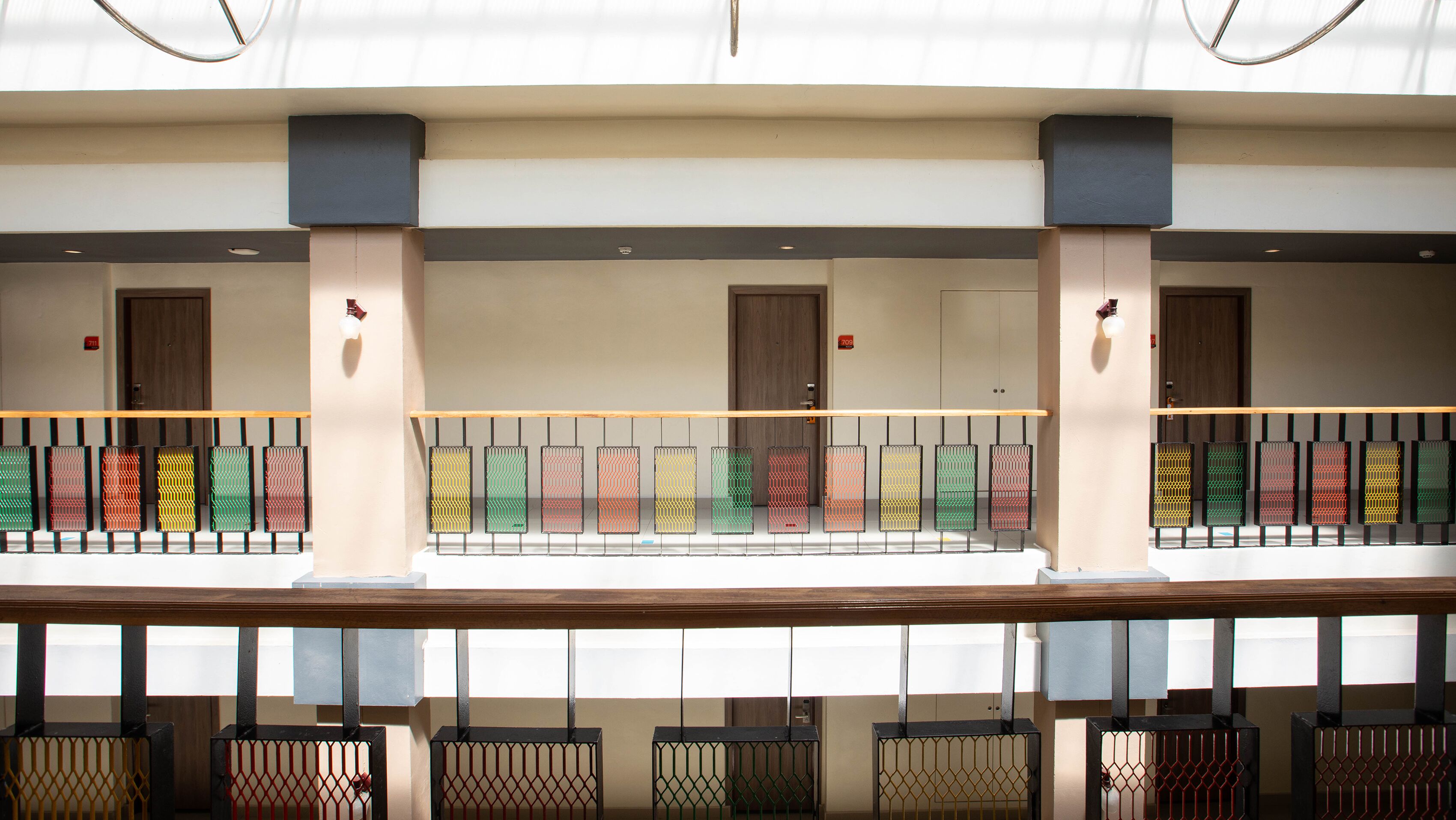 Un hall d’hôtel doté d’un long comptoir d’accueil, de plusieurs portes et d’un balcon orné de rampes aux couleurs vives.