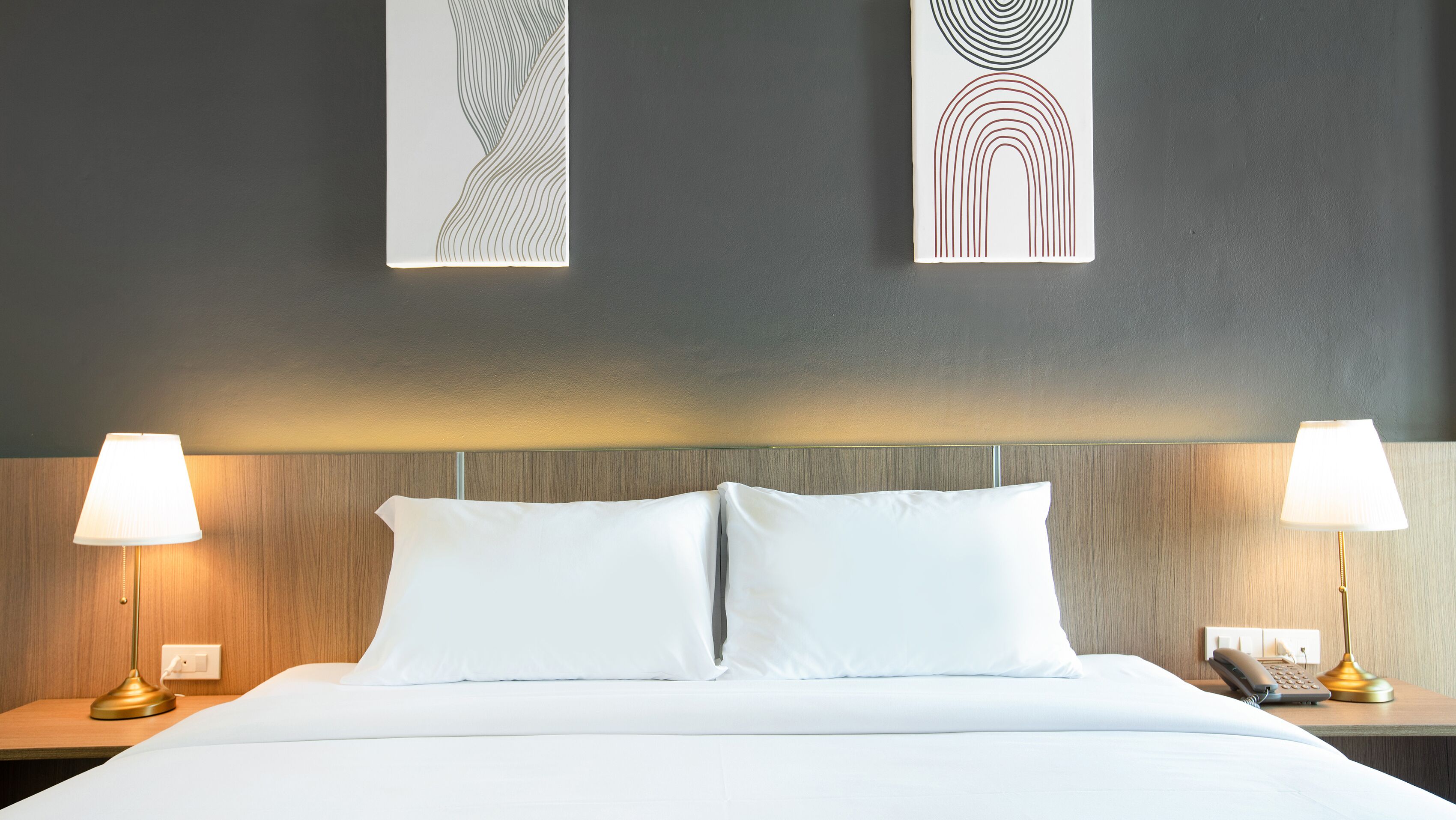 A hotel room with a large bed, two bedside lamps, a phone, and artwork on the wall.