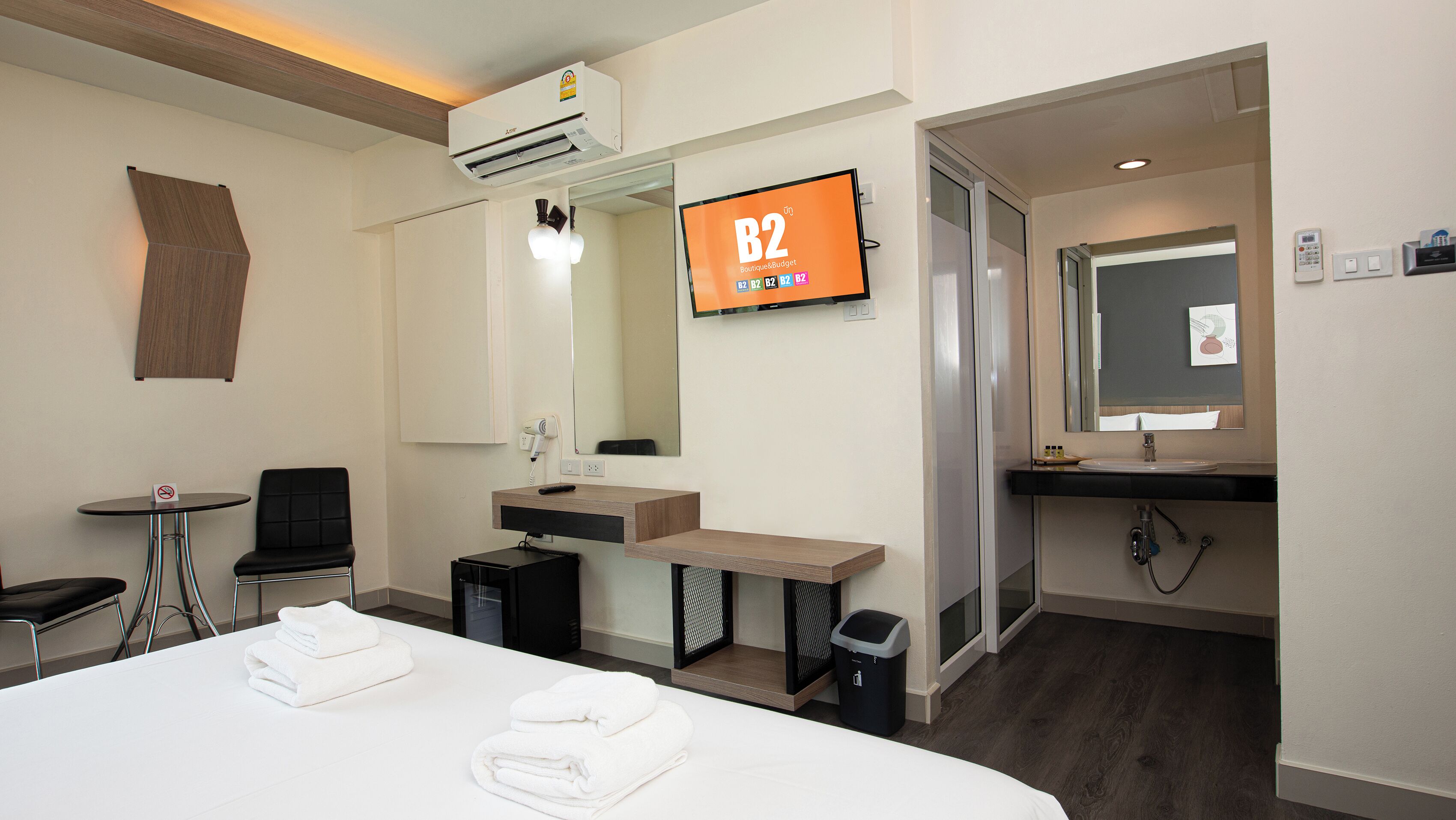 A hotel room with a bed, a desk, a chair, a TV, a mirror, and a bathroom.