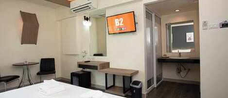 A hotel room with a bed, a desk, a chair, a TV, a mirror, and a bathroom.