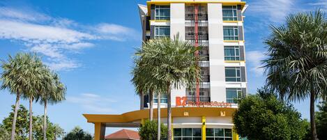 A modern hotel building with a 'B2' sign, featuring a yellow and white color scheme, surrounded by palm trees.