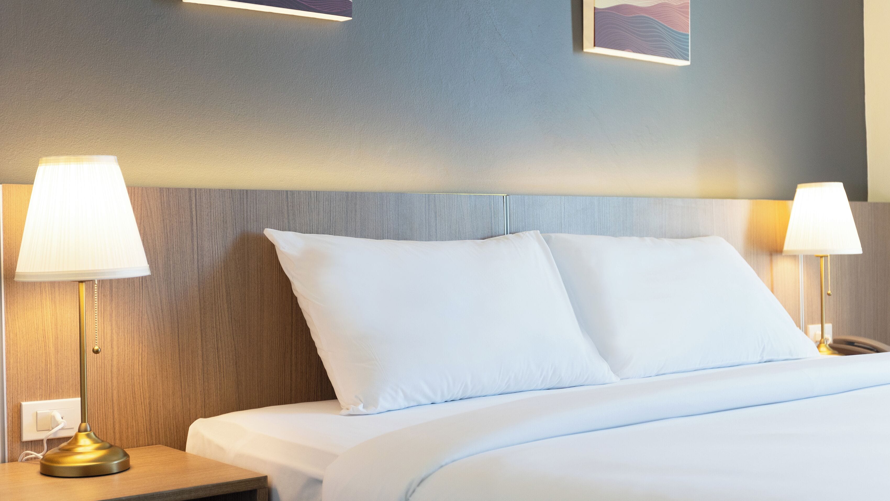 A hotel room with a bed, two bedside lamps, a nightstand, and a wall-mounted light fixture.