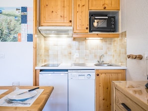 A compact kitchen with wooden cabinets, a built-in oven, a dishwasher, and a tiled backsplash.